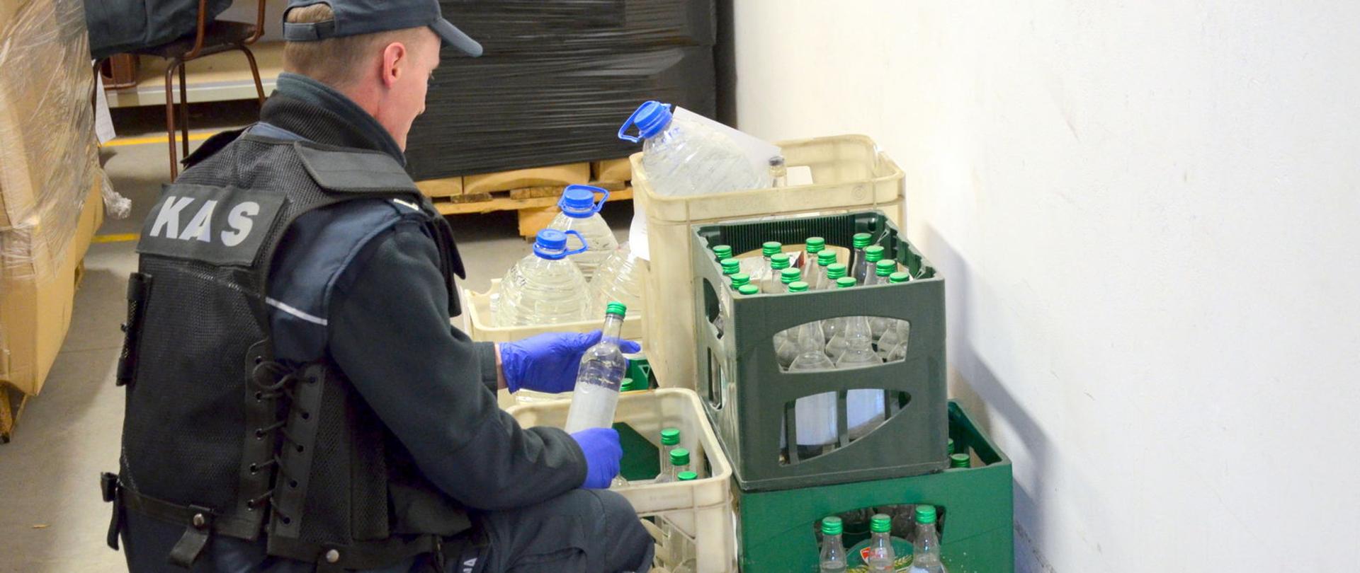 Funkcjonariusz KAS przy skrzyniach z butelkami z alkoholem.