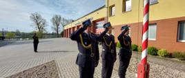 Funkcjonariusze KP PSP Międzychód podczas uroczystego podniesienia Flagi Rzeczpospolitej Polskiej. W tle budynek Komendy Państwowej Straży Pożarnej w Międzychodzie.