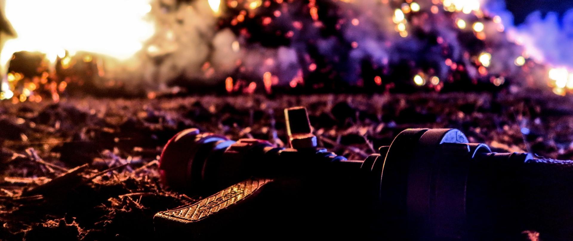 Na pierwszym planie gotowa do użycia prądownica wodna. W tle, dopalający się stos balotów.