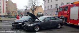 Na zdjęciu widnieją dwa pojazdy osobowe po kolizji oraz samochód pożarniczy w trakcie akcji. 