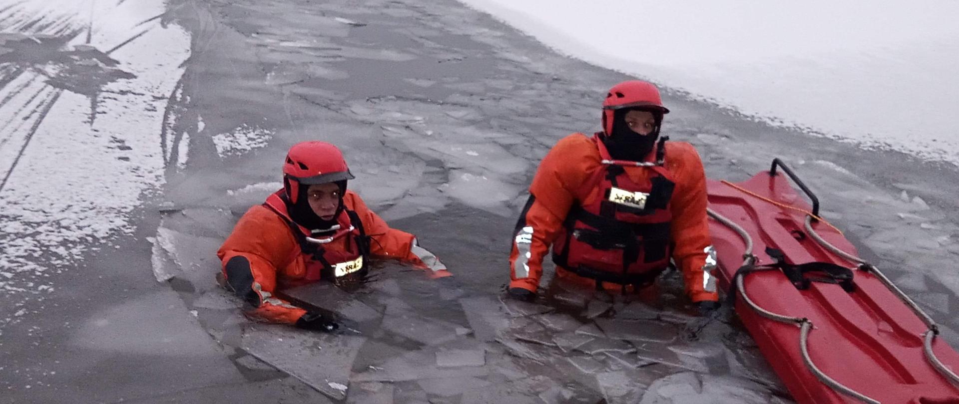 Dwóch strażaków w zamarzniętym zbiorniku wodnym obok deskosanie