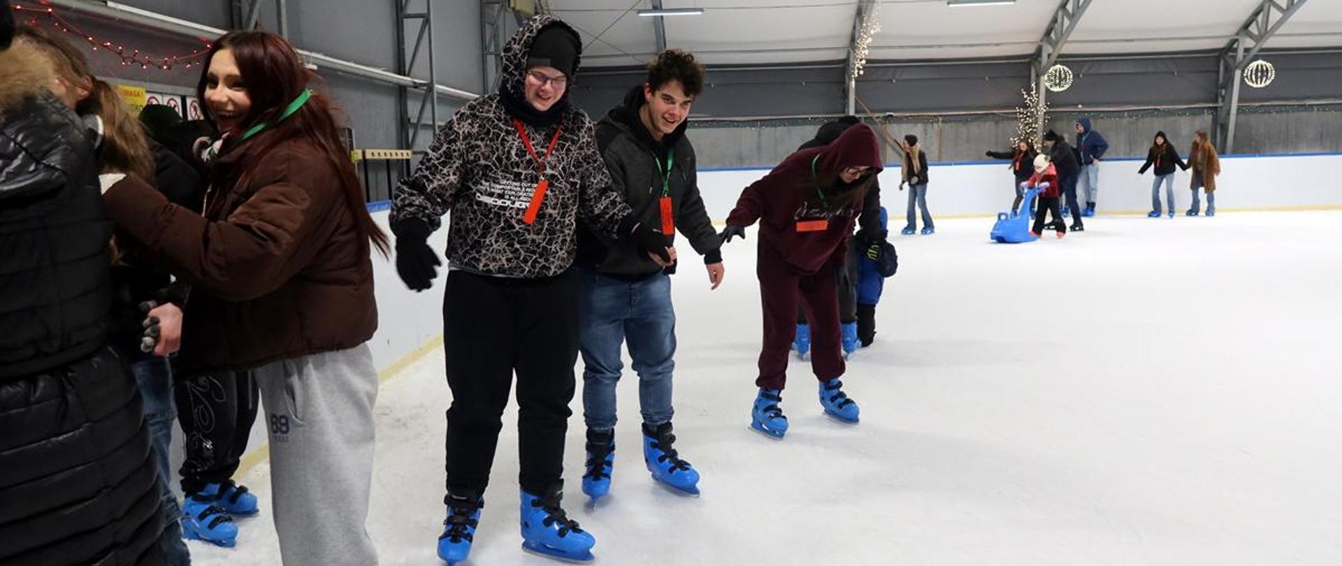 Uśmiechnięci młodzi ludzie jeżdżą na łyżwach na lodowisku krytym.