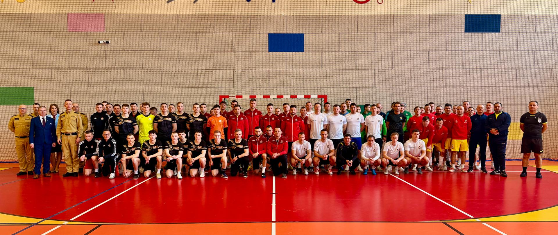 Zdjęcie drużyn ustawionych w szeregu podczas odprawy turniejowej, na hali sportowej.