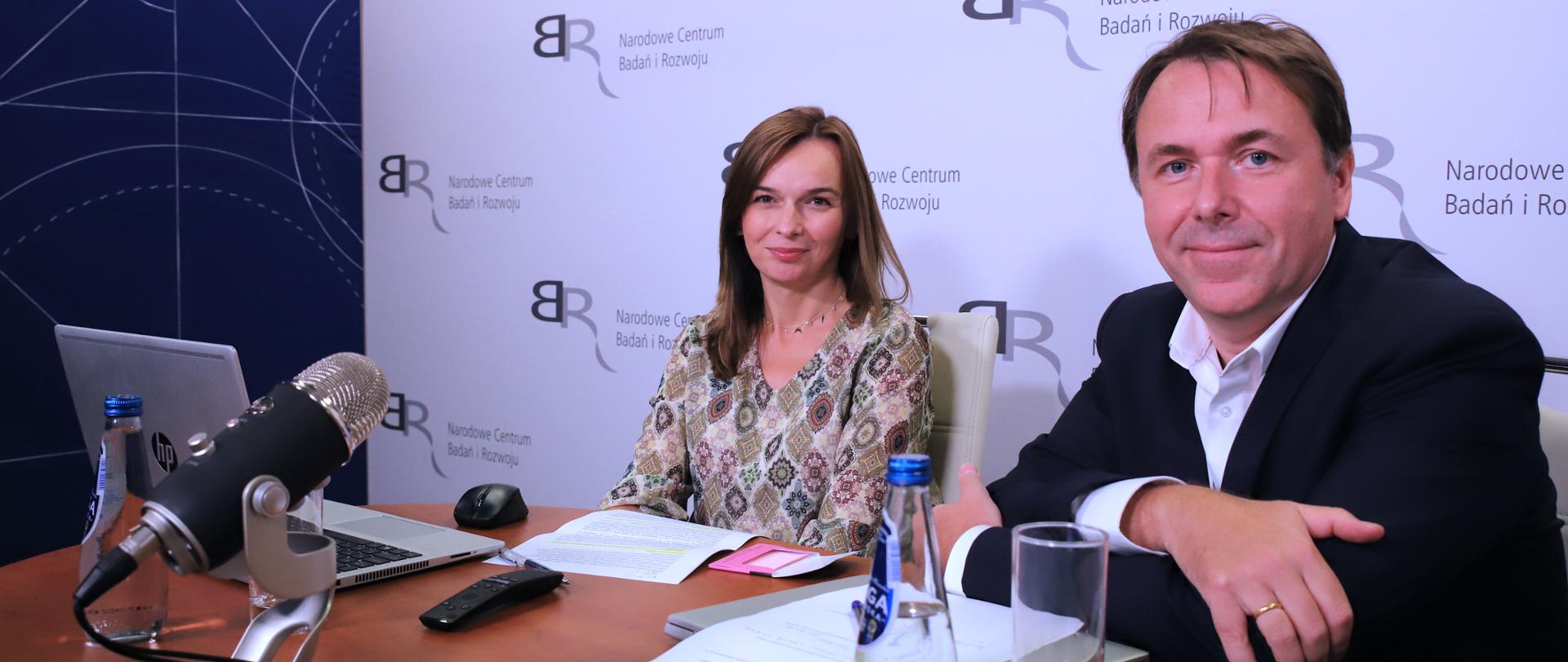 zdjęcie z wywiadu. w tle plansza z logotypem NCBR. osoby na zdjęciu od lewej Aneta Więcka - Kierownik projektu, Wojciech Racięcki, dyrektor Działu Rozwoju Innowacyjnych Metod Zarządzania Programami w Narodowym Centrum Badań i Rozwoju