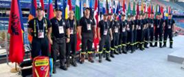 Strażacy którzy będą zabezpieczać Igrzyska stoją ustawieni do zdjęcia na tle flag krajów biorących udział w Igrzyskach 