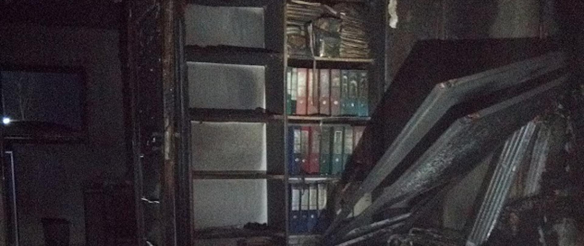 Wnętrze pomieszczenia biurowego po pożarze. Wszystkie elementy wyposażenia okopcone i częściowo nadpalone.