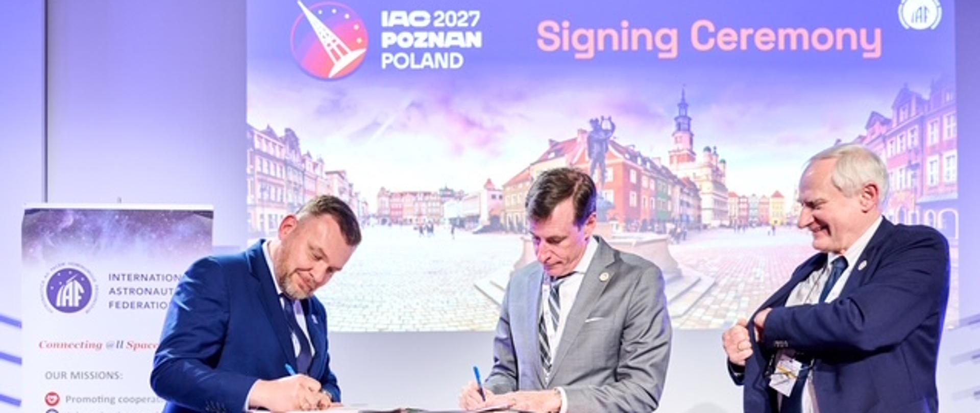 Dwie osoby podpisują dokument, obok stoi trzecia