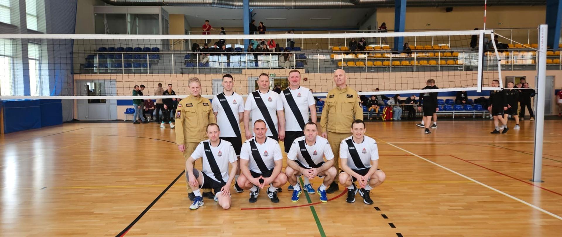 Zdjęcie pamiątkowe drużyny KP PSP Mława z kierownictwem. Na hali sportowej pod siatką.