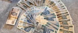 Na blacie stołu leży dużo banknotów o nominałach 50, 100 i 200 złotych.