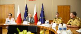 Wojewoda opolska, minister Siemoniak, dwaj komendanci PSP siedzą przy okrągłym stole. W tle flagi polskie i unijne. 
