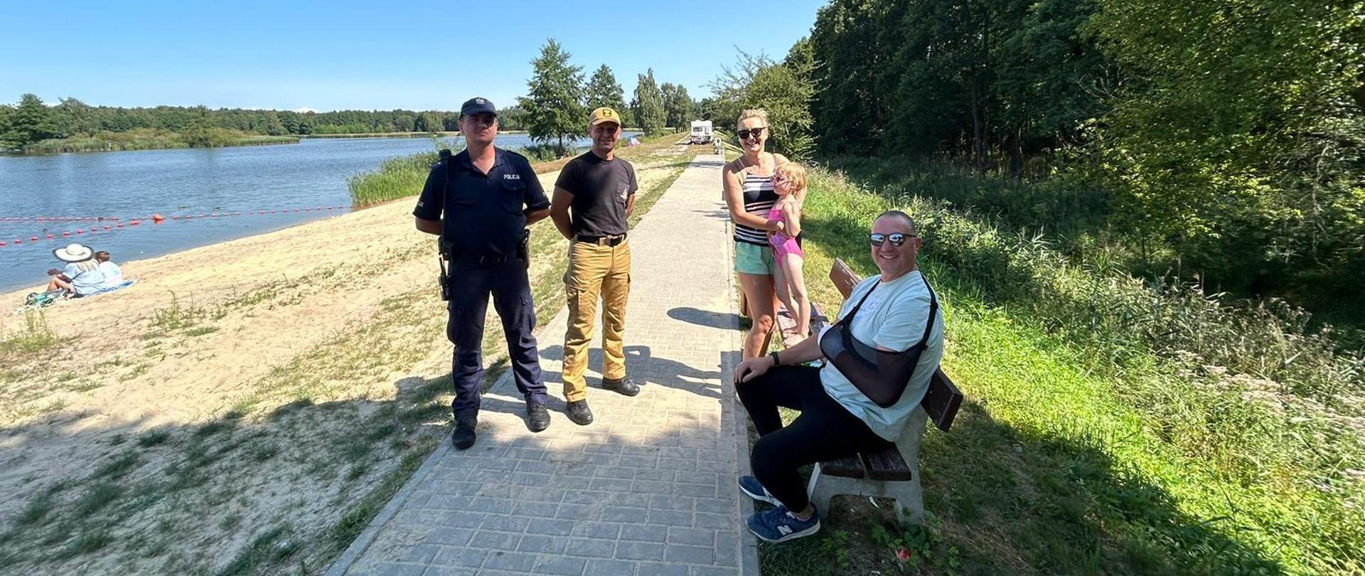 Teren zbiornika wodnego Klekot, plaża rejon kąpieliska, na wodzie wyznaczono obszar dopuszczony do kąpieli, na plaży znajdują się dzieci i ich opiekunowie wraz z funkcjonariuszami Policji oraz Państwowej Straży Pożarnej.