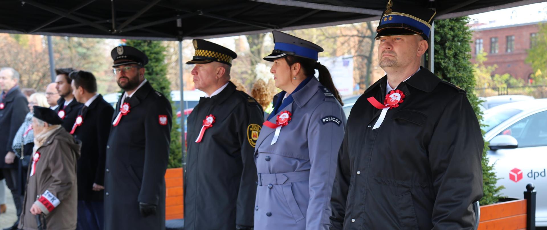 W rzędzie stoją obok siebie komendant powiatowy PSP, komendant powiatowy policji oraz komendant miejski straży miejskiej. Do płaszczy przyczepione mająkotyliony w barwach narodowych