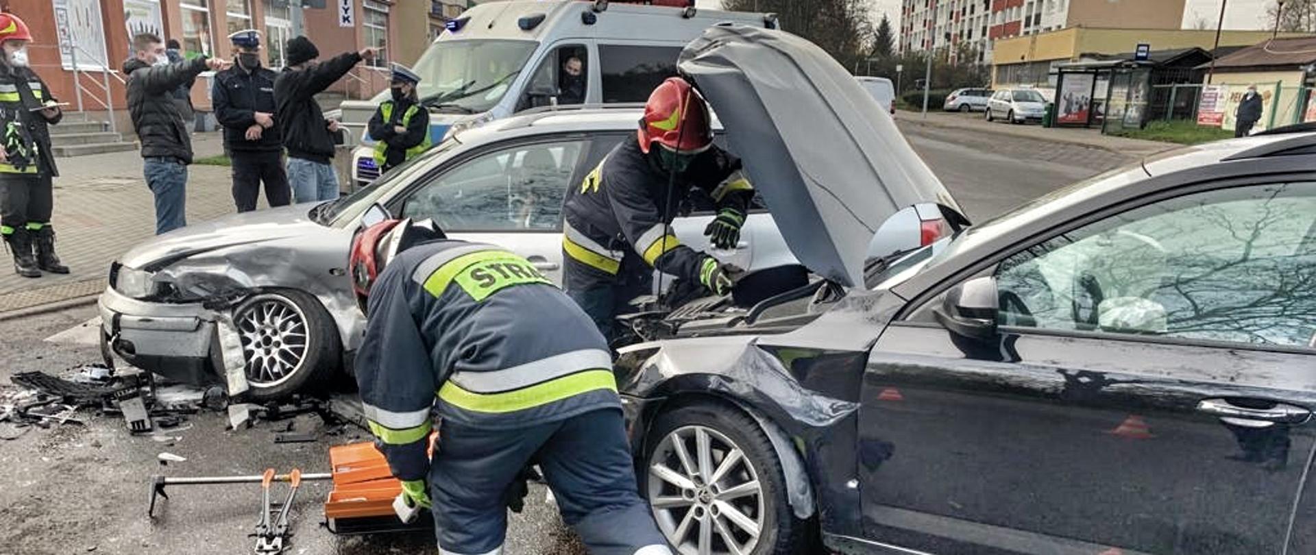 Kolizja dwóch samochodów osobowych. Strażacy odłączają akumulator w jednym z pojazdów.
