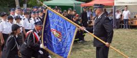 Na zdjęciu widzimy uroczyste ucałowanie sztandaru przez przedstawiciela Ochotniczej Straży Pożarnej w Świeżawach. W tle widać stojących w dwuszeregu członków OSP Świeżawy oraz przybyłych na uroczystość gości i mieszkańców.