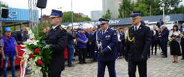 Zastępca pomorskiego komendanta wojewódzkiego Państwowej Straży Pożarnej, zastępca komendant wojewódzkiego Policji idą za strażakiem trzymającym wieniec. 