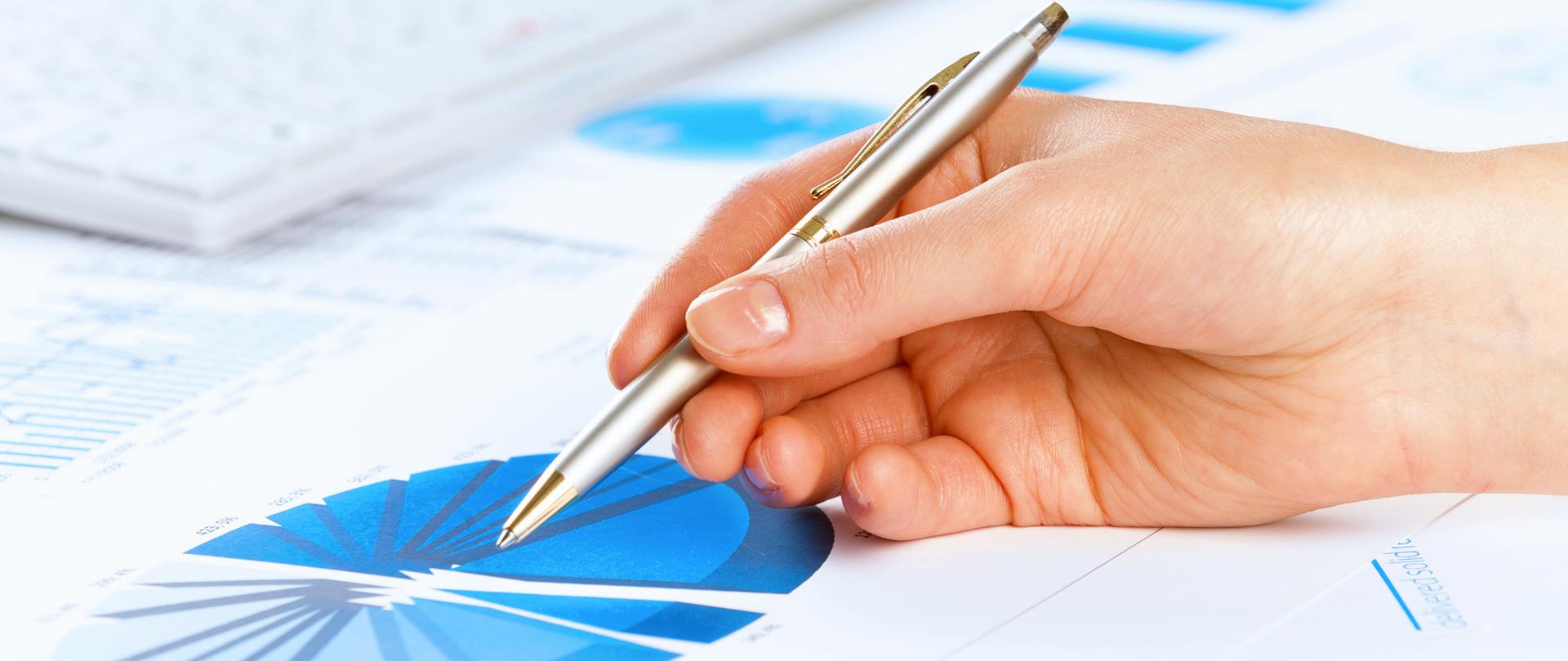 Wykres kołowy i dłoń z długopisem - zdjęcie ilustracyjne