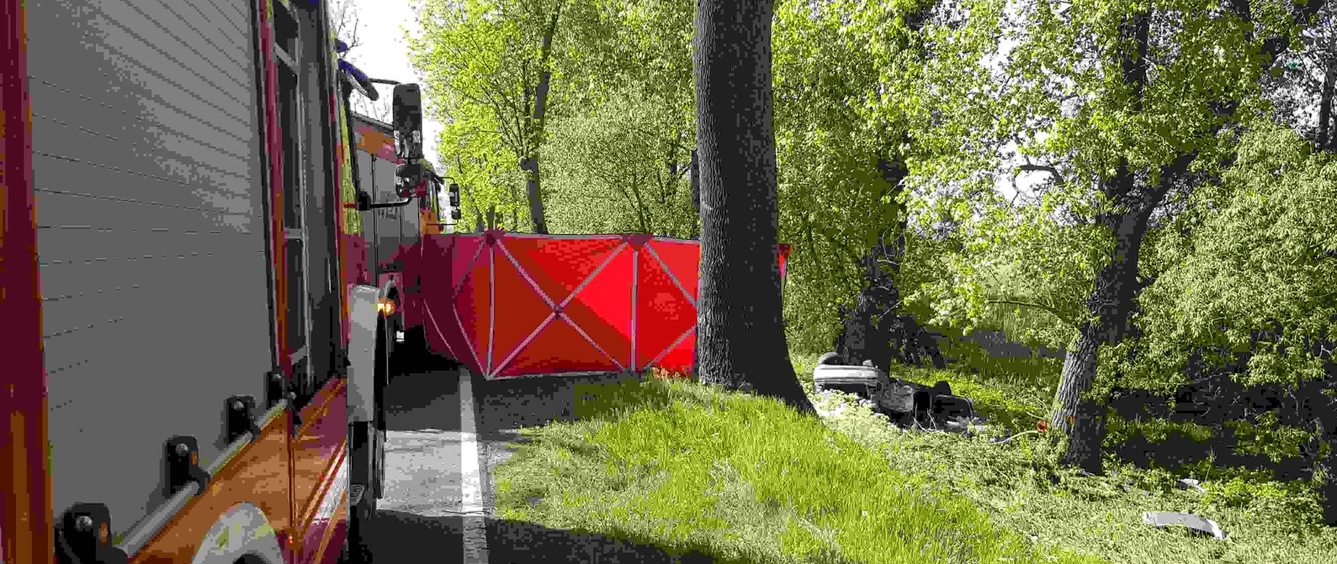 Pojazd strażacki i zniszczony pojazd leżący w rowie