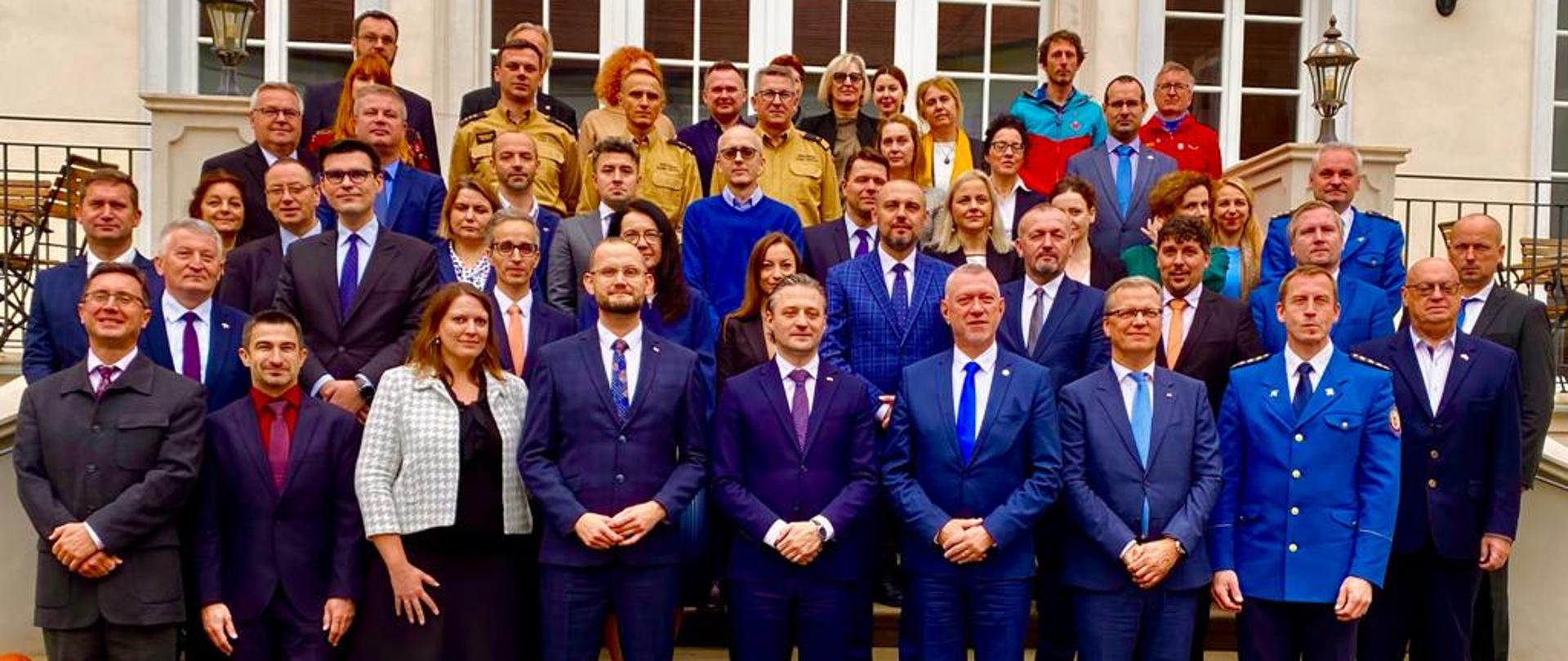 Na zdjęciu znajdują się zastępca komendanta głównego PSP nadbryg. Krzysztof Hejduk, podsekretarz stanu w MSWIA Bartosz Grodecki, przedstawiciele KW PSP Kraków, Katarzyna Borysiuk-Czapla BOL KG PSP oraz uczestnicy posiedzenia pozują do zdjęcia stojąc przed wejściem do budynku w którym odbywało się posiedzenie