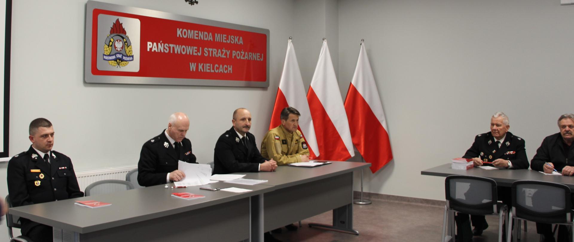 Zdjęcie przedstawia siedzących za stołem prezydialnym od lewej: dh Piotr Biegański, dh Ireneusz Żak, pan Mariusz Ściana i bryg. Mariusz Góra