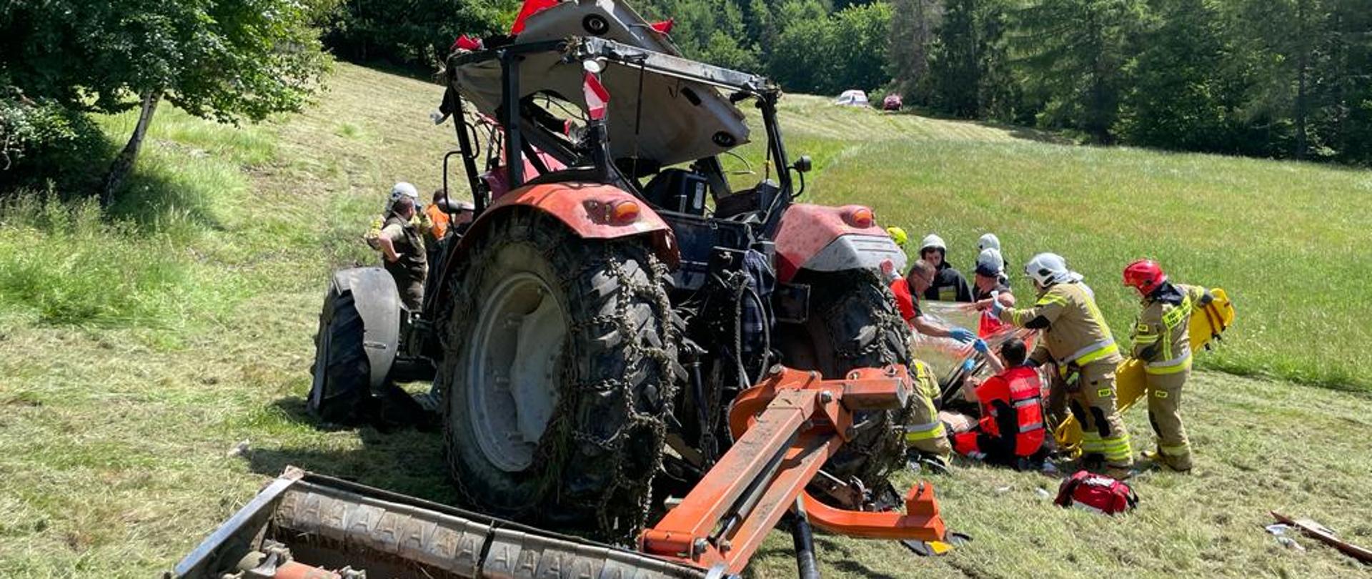 Uszkodzony ciągnik rolniczy a obok strażacy
