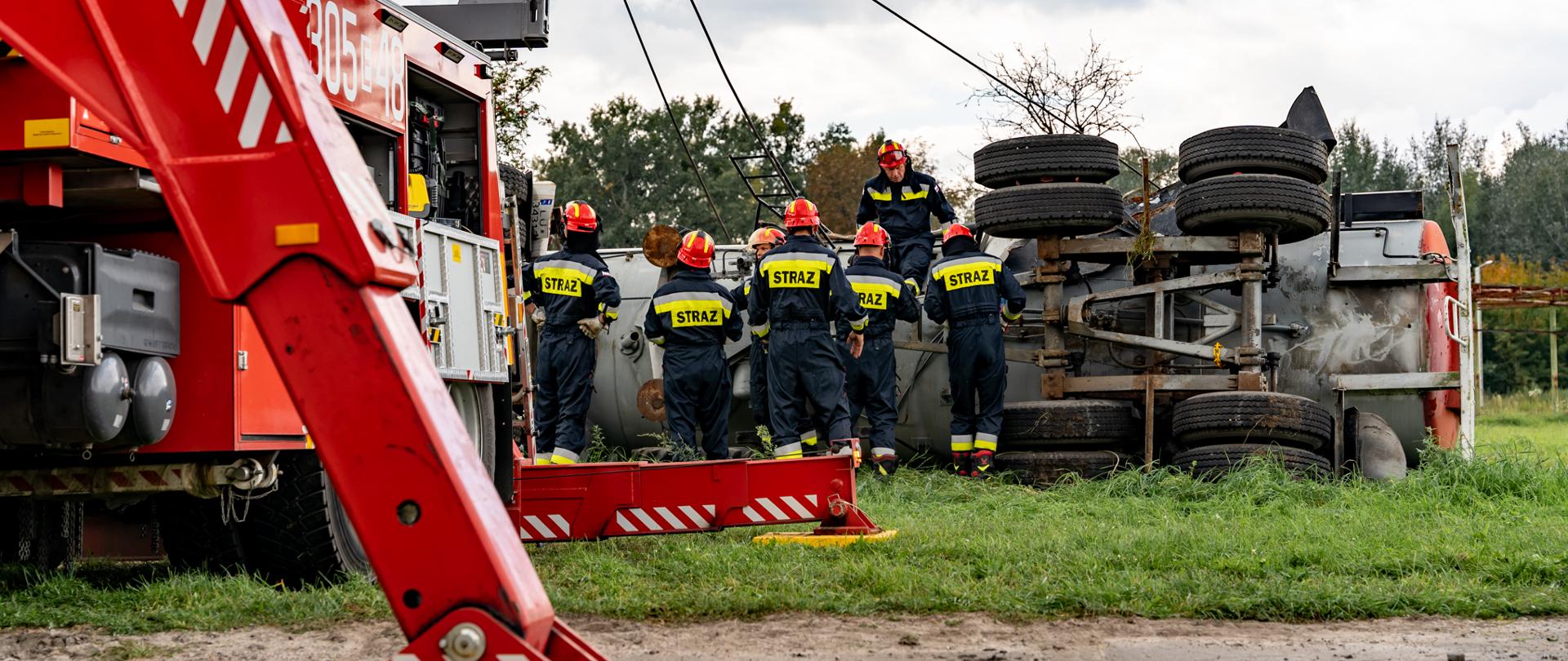 Ciężki samochód ratownictwa technicznego, w tle strażacy pracujący przy przewróconej cysternie