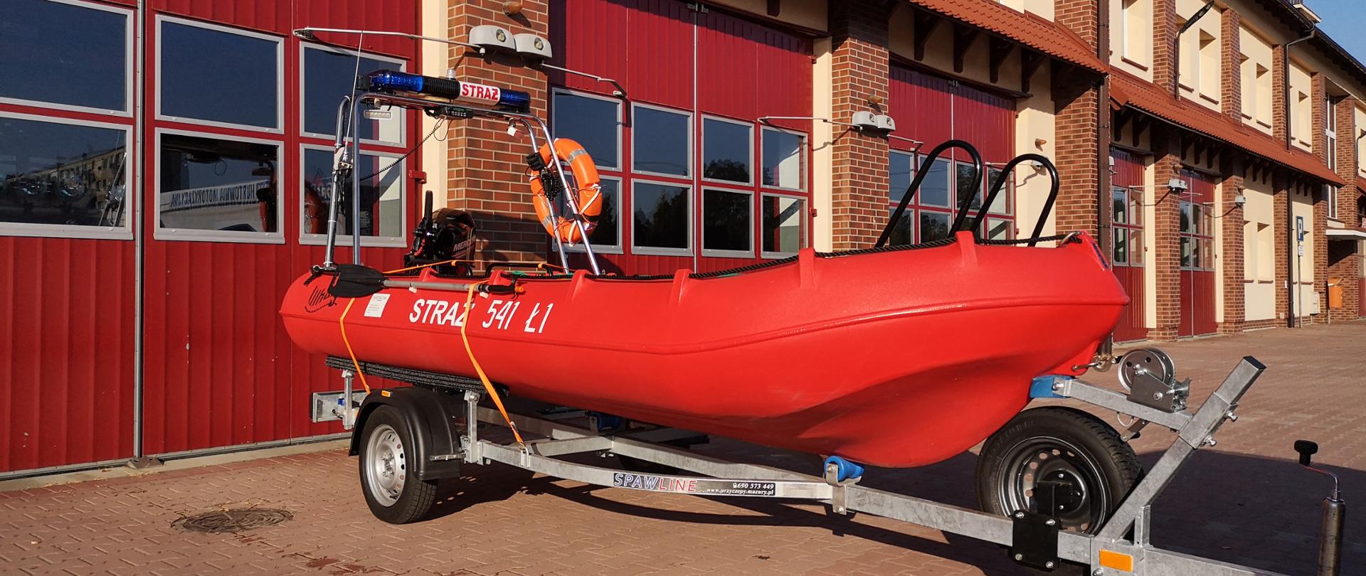 Na zdjęciu łódź ratownicza Whaly zamocowana do przyczepki transportowej. Zdjęcie wykonane na placu manewrowym przed garażami Jednostki Ratowniczo-Gaśniczej
