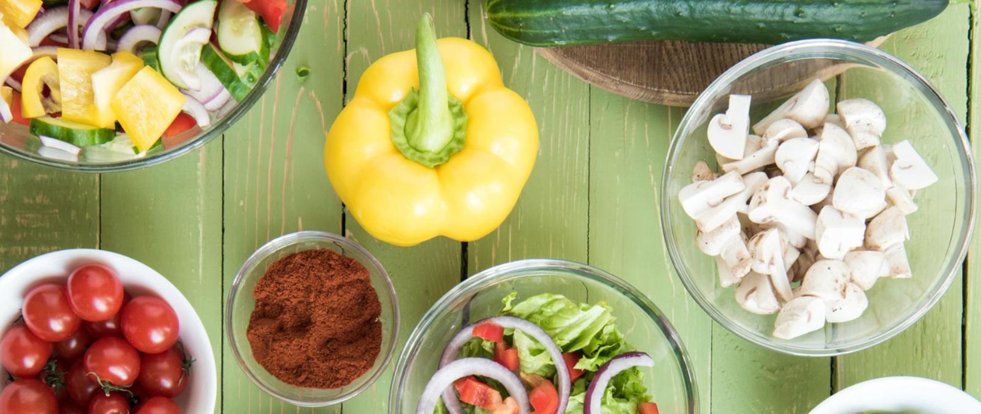 Na zdjęciu są warzywa i przyprawy znajdujące się na zielonym drewnianym blacie.