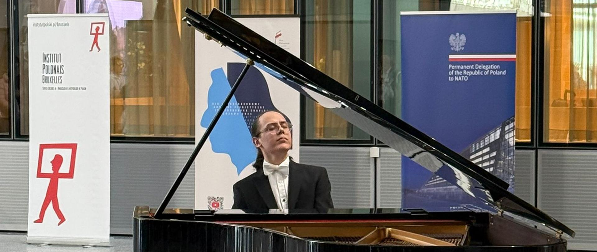A man in a tailcoat plays the piano against the backdrop of the logos of the Polish Institute, the Fryderyk Chopin Institute and Polish Delegation to NATO