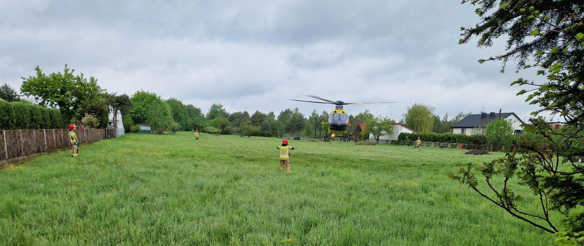 Helikopter lądujący na polu, strażacy wyznaczają miejsce lądowania
