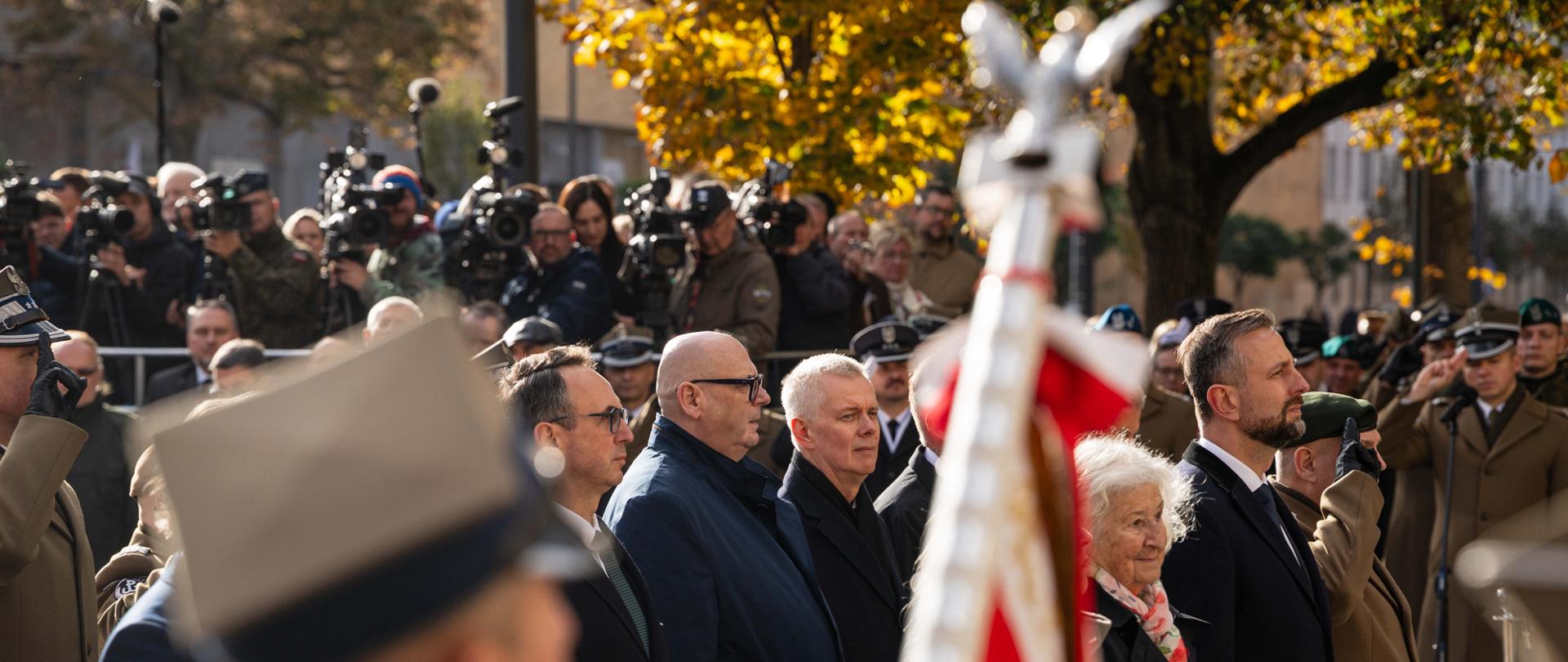 Na zdjęciu uroczystość odsłonięcia pomnika generała broni Tadeusza Jordan Rozwadowskiego. Zdjęcie przedstawia zaproszonych gości oraz żołnierzy Wojska Polskiego. Wśród gości m.in. minister Tomasz Siemoniak oraz wicepremier Władysław Kosiniak-Kamysz. Na drugim planie po lewej stronie widać strefę medialną ze stojącymi operatorami kamer, fotoreporterami oraz dziennikarzami. Z prawej strony zdjęcia w tle duże drzewo. Na pierwszym planie widać fragment sztandaru wojskowego i głowy żołnierza. 
