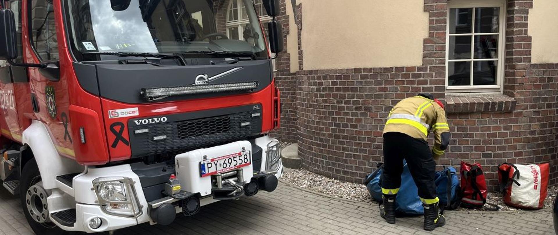 Wóz strażacki oraz strażak, który przygotowuje sprzęt do ratownictwa wysokościowego