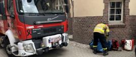 Wóz strażacki oraz strażak, który przygotowuje sprzęt do ratownictwa wysokościowego