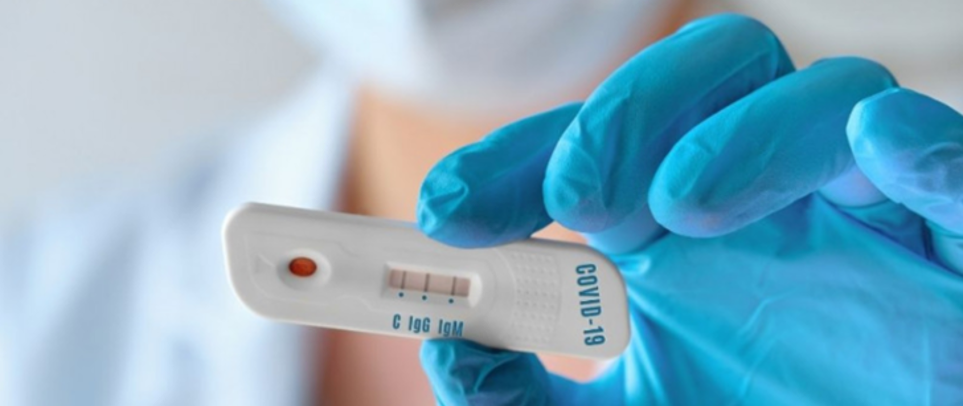 Na zdjęciu ręka w rękawiczce niebieskiej trzymająca test z napisem COVID-19