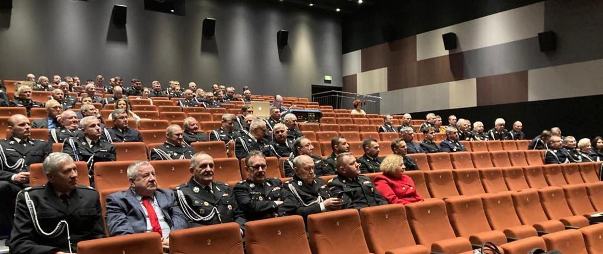 W sali widowiskowej siedzą strażacy oraz osoby cywilne