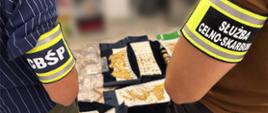 Funkcjonariusze podczas kontroli, oglądają zabezpieczoną biżuterię i metale szlachetne ułożone na tackach.