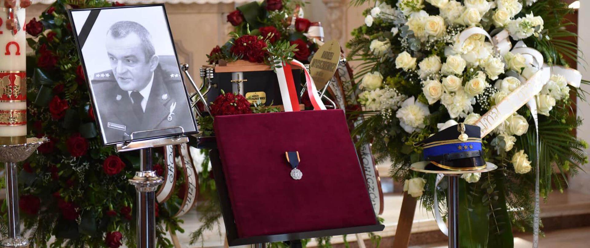 urna, zdjęcie z kirem, rogatywka, medal i wieńce pogrzebowe