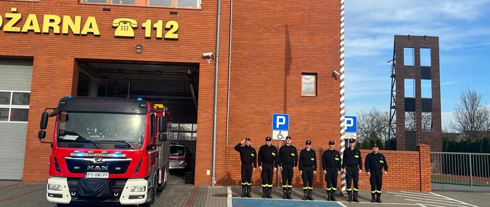 Strażacy na tle masztu flagowego śpiewają hymn narodowy