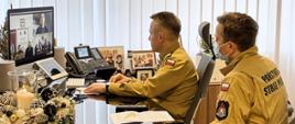 Komendant Główny PSP wraz z drugim funkcjonariuszem siedzą przy biurku przy monitorze ekranowym podczas wideokonferencji