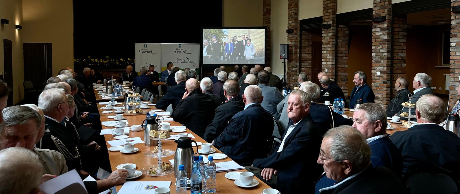 Uroczystość wręczenia decyzji. Przy stole siedzą przedstawiciele jednostek OSP, którzy otrzymali świadczenia. Na ekranie wyświetlana jest prezentacja.