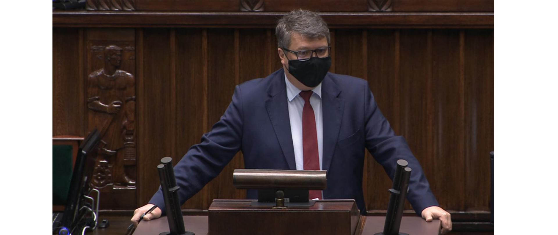 Na zdjęciu widać wiceministra MSWiA Macieja Wąsika stojącego na mównicy sejmowej i przemawiającego.