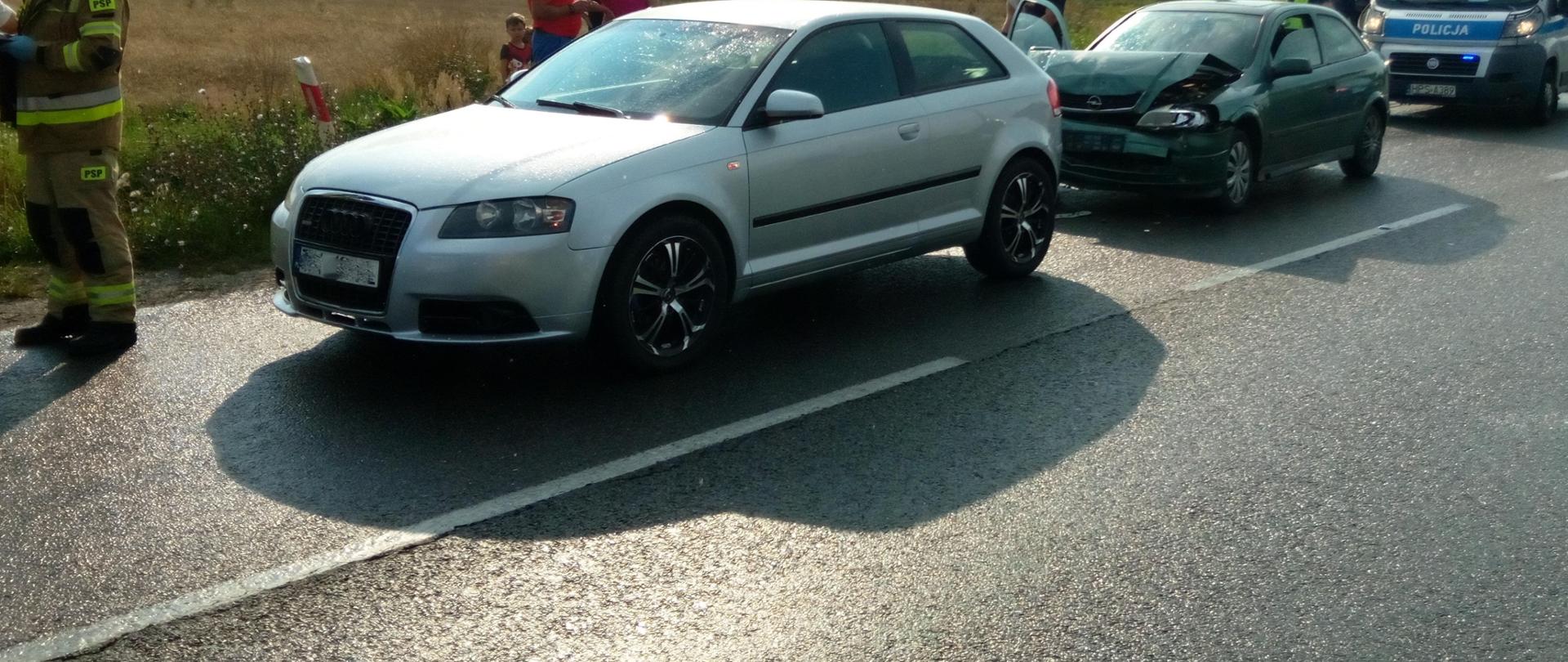 Zdjęcie przedstawia dwa z trzech aut biorących udział w wypadku komunikacyjnym. Za pojazdami widać radiowóz policyjny.