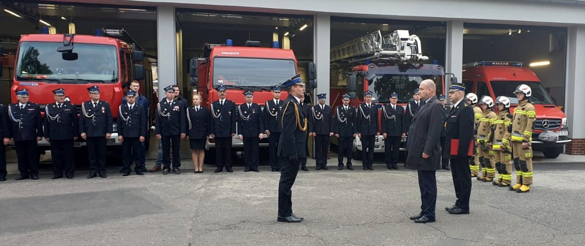 UROCZYSTE WRĘCZENIE PROMES ORAZ PRZEKAZANIE SAMOCHODU. Na zdjęciu widzimy zaproszonych gości oraz strażaków zebranych na uroczystości, w tle samochody strażackie w bramach strażnicy i budynek Komendy.