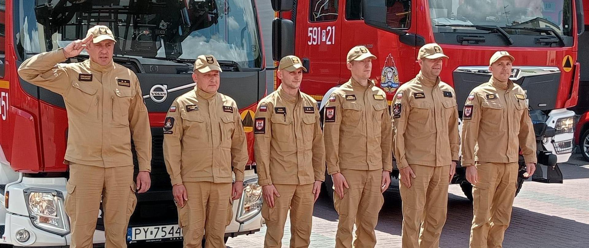 Strażacy oddają hołd przy samochodach strażackich