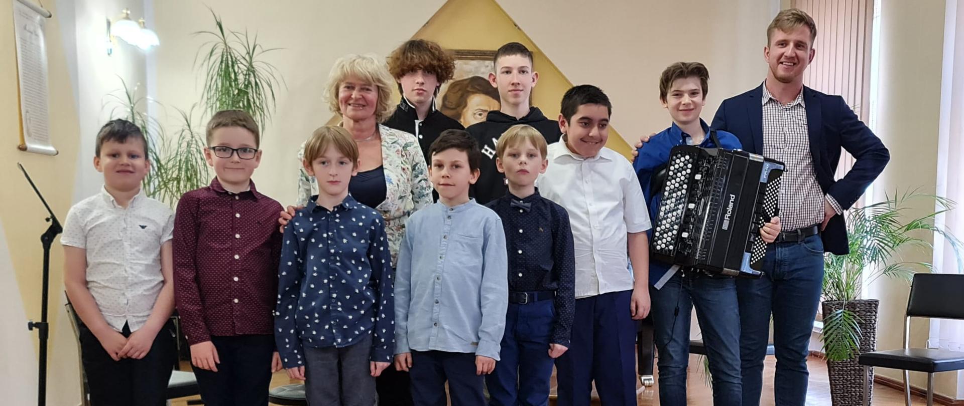 Grupa uczniów wraz z nauczycielami L. Stopką i T. Brusińskim na zdjęciu grupowym w auli PSM I st. w Kłodzku, poniżej ułożone są akordeony.