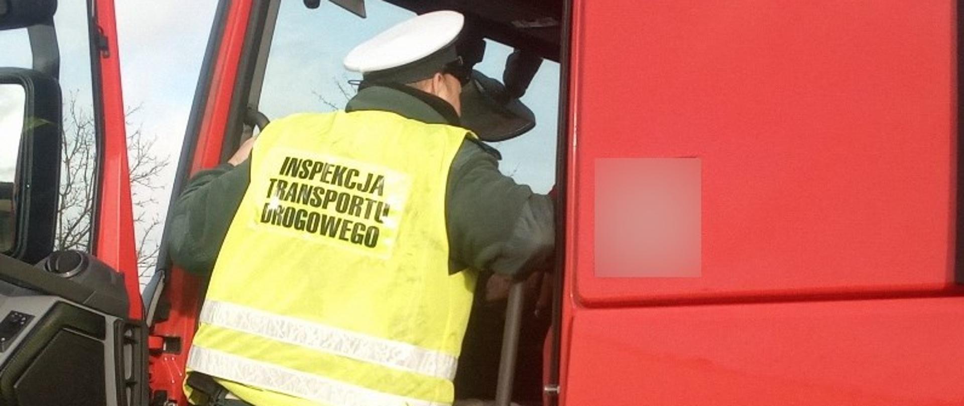 Inspektor ITD stoi w wejściu do kabiny ciężarówki od strony kierowcy i pobiera dokumenty do kontroli drogowej.
