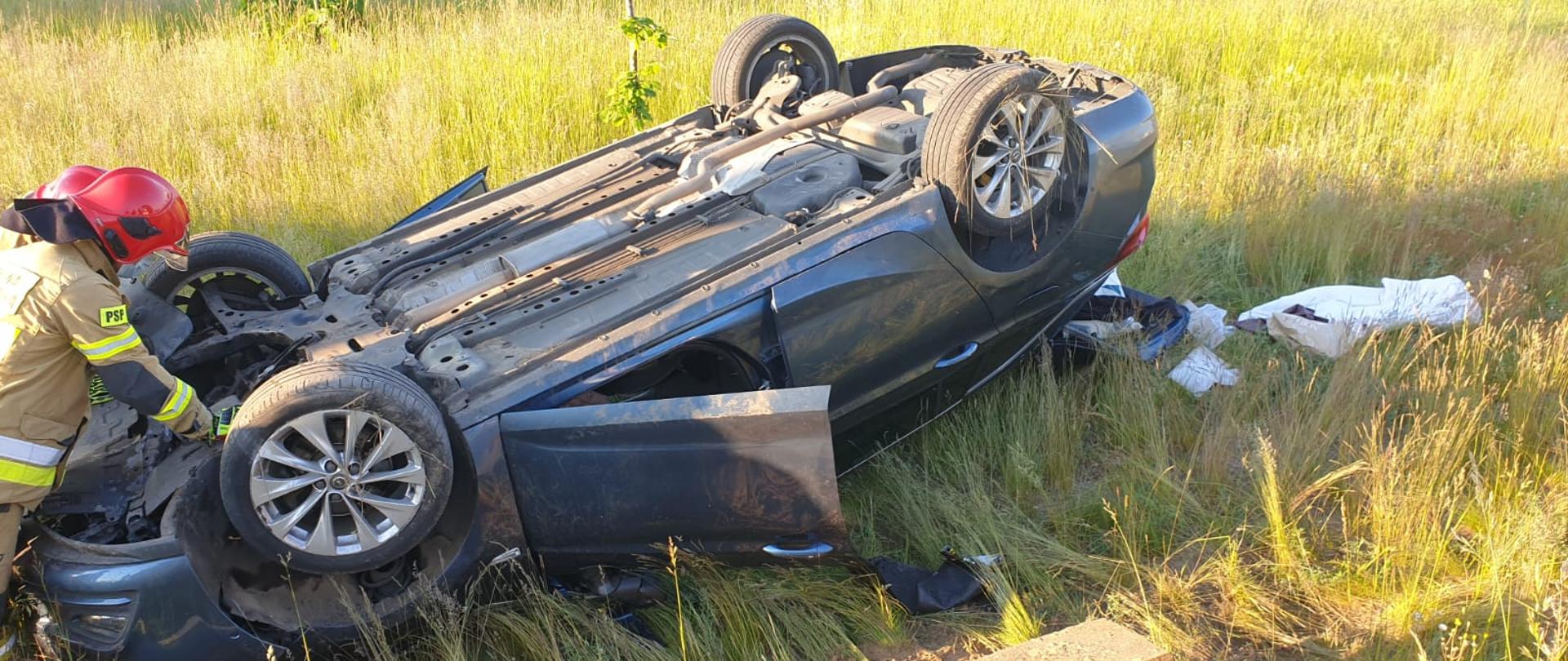 Zdjęcie przedstawia pojazd Opel Astra leżący na dachu. Dwóch strażaków z JRG Międzyrzecz prowadzi czynności zabezpieczające pojazd.