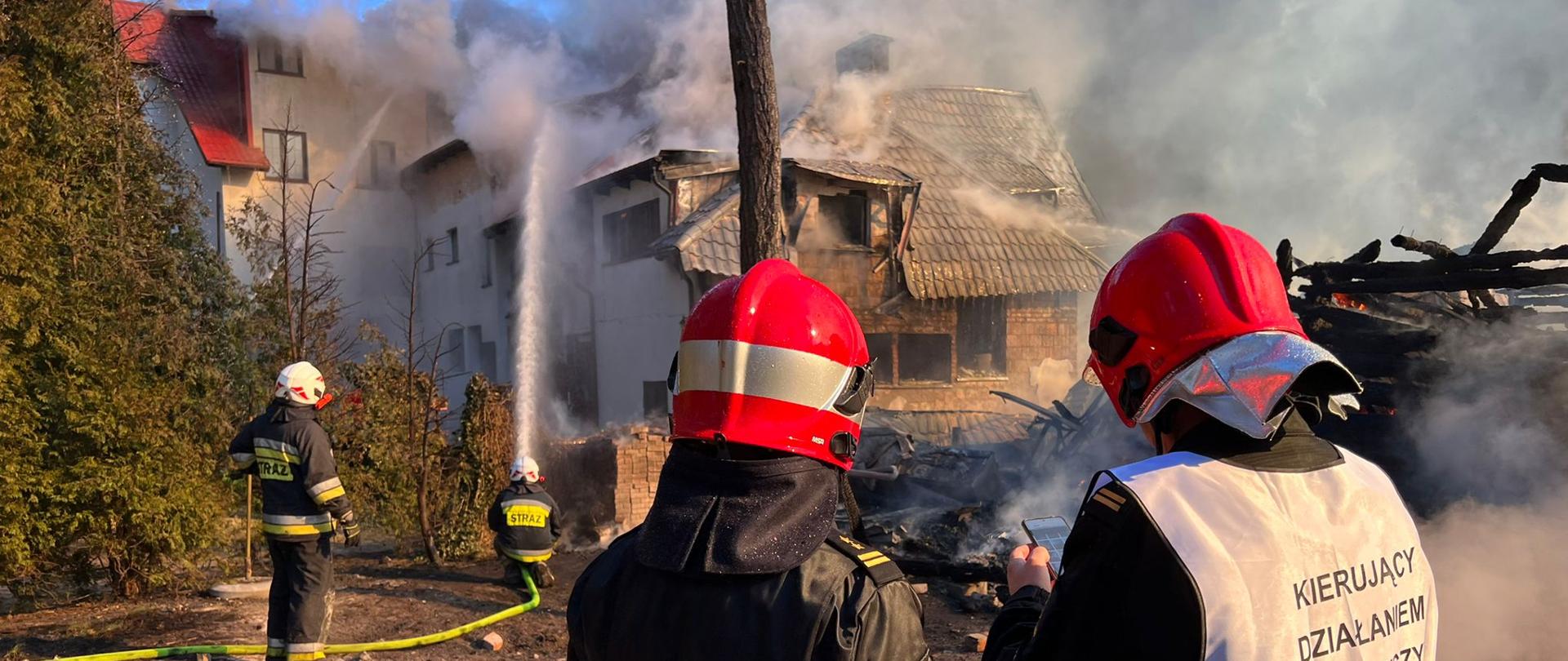 Zdjęcie przedstawia pożar obiektu hotelowego. Na zdjęciu widoczna rota podająca prąd wody na dach obiektu oraz kierującego działaniem ratowniczy.