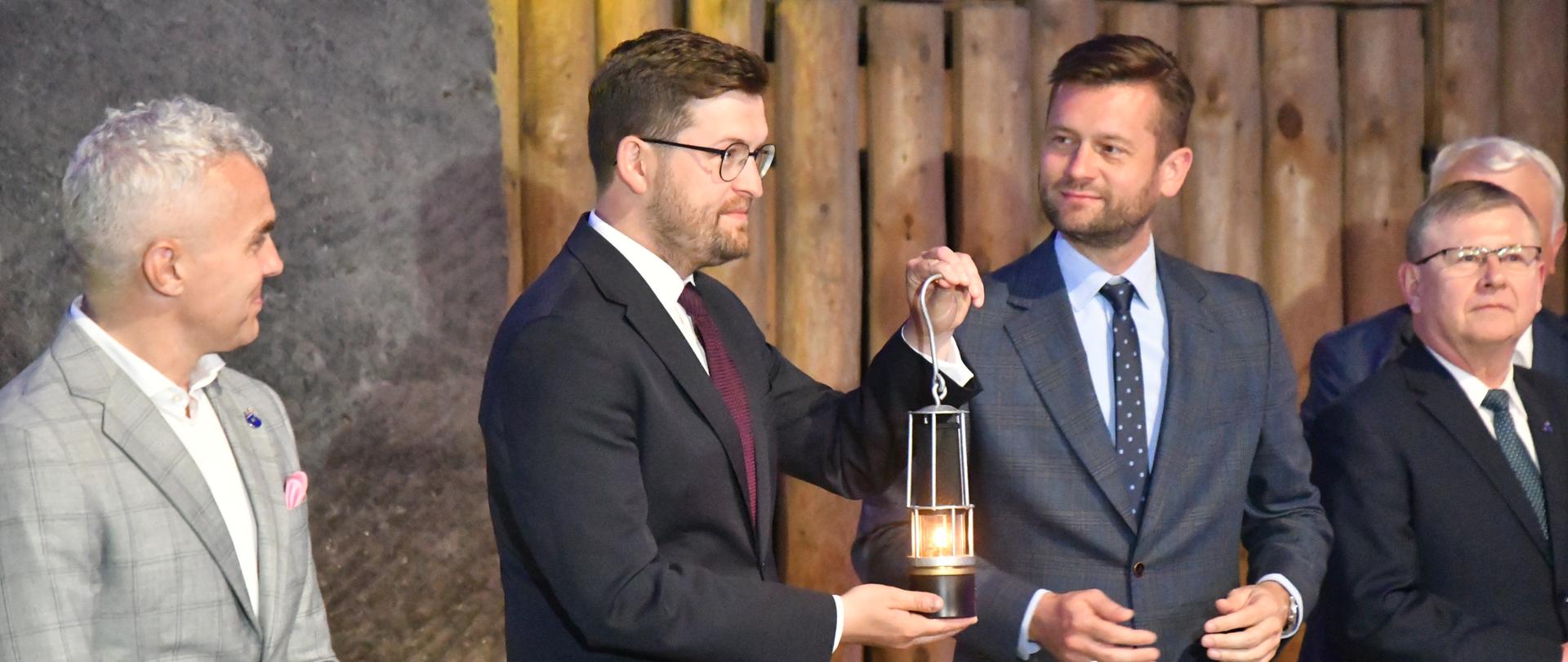 Wiceminister Andrzej Śliwka oraz minister sportu i turystyki Kamil Bortniczuk z Ogniem Pokoju. Obok stoją mężczyźni. 