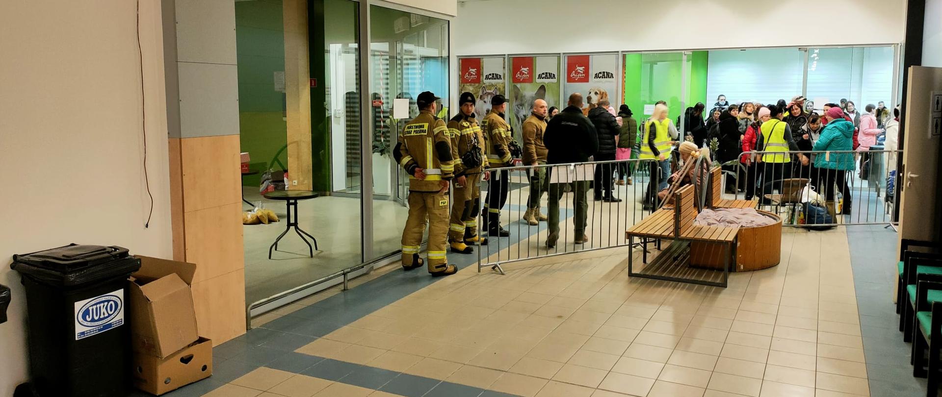 Strażacy w budynku, w wejściu uchodźcy z Ukrainy 