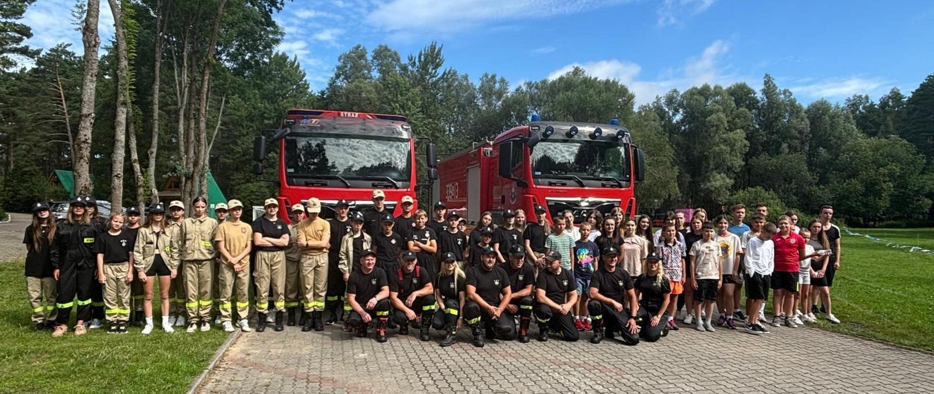Na zdjęciu uczestnicy obozu wraz z opiekunami na tle dwóch wozów strażackich.